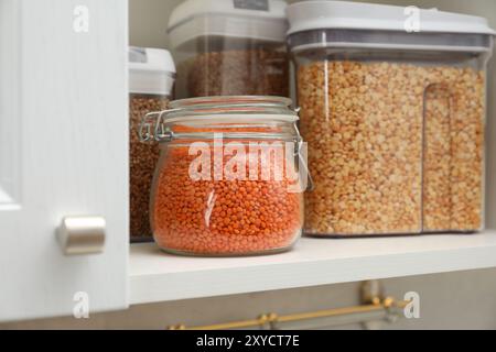 Verschiedene Arten von Getreide und Hülsenfrüchten in Behältern im Schrank, Nahaufnahme Stockfoto