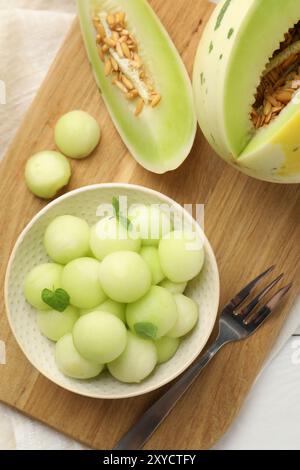 Melonenkugeln in der Schüssel und frisches Obst auf weißem Holztisch, Blick von oben Stockfoto