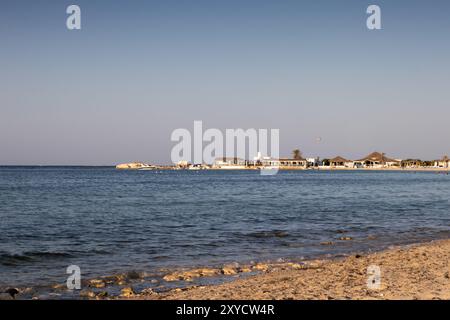 Strand eines Resorts in einer goldenen Stunde. Blick auf das ruhige Mittelmeer und eine Architektur an der Küste. Klarer blauer Himmel im Sommer. Djerba Stockfoto