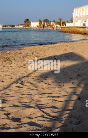 Strand eines Resorts in einer goldenen Stunde. Blick auf das ruhige Mittelmeer und eine Architektur an der Küste. Klarer blauer Himmel im Sommer. Djerba Stockfoto