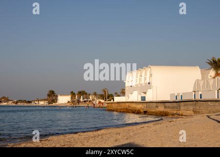 Strand eines Resorts in einer goldenen Stunde. Blick auf das ruhige Mittelmeer und eine Architektur an der Küste. Klarer blauer Himmel im Sommer. Djerba Stockfoto