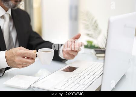 Geschäftsmann trinkt Kaffee bei der Arbeit und spricht online Stockfoto