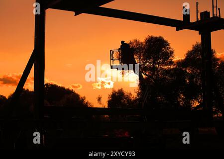 Mann, der bei Sonnenuntergang auf einer Gabelstaplerplattform steht, während der Bau der Saint Barbara-Brücke stattfindet Stockfoto