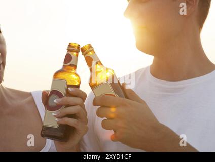 Paare am Strand feiern, trinken und Spaß im Sonnenuntergang haben, Flaschen in den Händen halten, während die Sonne durchscheint Stockfoto