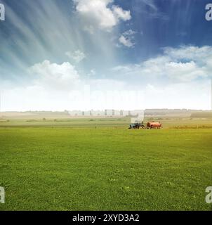 Traktor auf grünem Feld über blauem, bewölktem Himmel ernten im Sommer oder Herbst Stockfoto