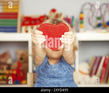 Glückliches Kind mit kleinem, handgemachtem rotem Herzen aus Papier in der Klasse. Valentinstag-Konzept Stockfoto