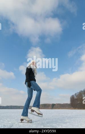 Junge Frau, die auf einem gefrorenen See in Mecklenburg Schlittschuhlaufen geht. Blick von unten, Weitwinkel für besondere Wirkung. Junge Frau, die auf einem gefrorenen See Schlittschuhlaufen läuft, lustig Stockfoto