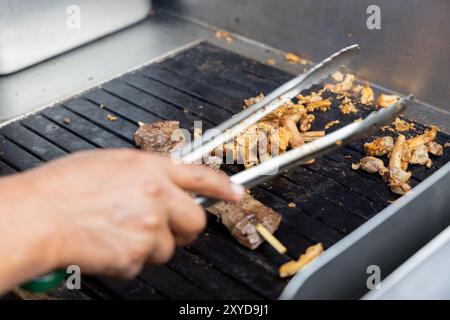 Eine Person kocht Antikuchos auf einem Grill. Das Fleisch wird auf Spießen gekocht und wird von anderem Fleisch umgeben Stockfoto