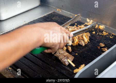 Eine Person kocht Antikuchos auf einem Grill. Das Fleisch wird auf Spießen gekocht und wird von anderem Fleisch umgeben Stockfoto