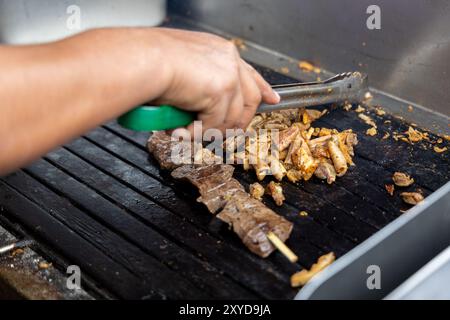 Eine Person kocht Antikuchos auf einem Grill. Das Fleisch wird auf Spießen gekocht und wird von anderem Fleisch umgeben Stockfoto