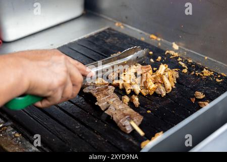 Eine Person kocht Antikuchos auf einem Grill. Das Fleisch wird auf Spießen gekocht und wird von anderem Fleisch umgeben Stockfoto