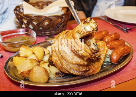 Gebratene Schweinshaxe mit Bratkartoffeln und Würstchen aus Metall Platte Stockfoto