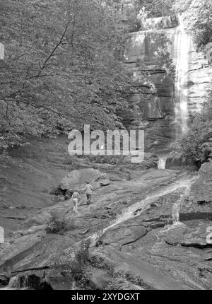 Eine kaukasische Frau und ein Junge klettern auf Felsen an einem malerischen Wasserfall in der Nähe von Brevard, North Carolina, USA. Stockfoto