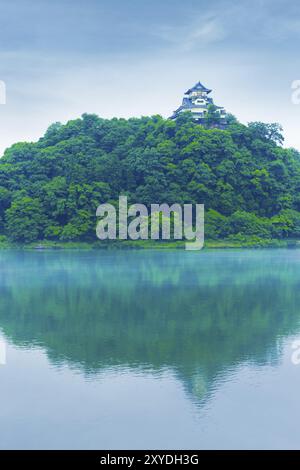 Die Fassade des Inuyama-Schlosses aus der Ferne hoch über dem Waldberg spiegelt sich am Tag des blauen Himmels in der Präfektur Gifu, Japan, im Wasser des Kiso-Flusses. Vertikaler Cop Stockfoto