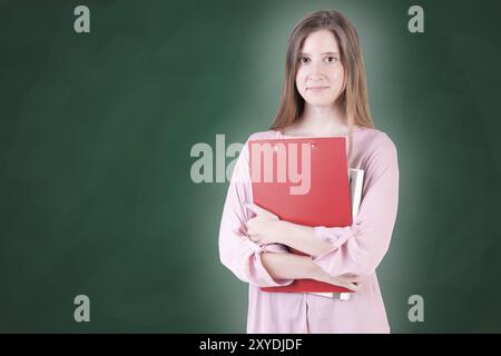 Junge Frau mit Notebooks auf dem Arm, in einem grünen Tafel-Hintergrund Stockfoto