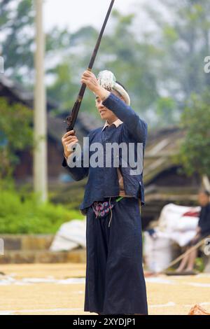 Biasha, China, 17. September 2007: Miao ethnische Minderheit in traditioneller blauer Kleidung, geflochtenem Kopfschmuck und langem Haarbutt, der eine Waffe in die Luft schießt Stockfoto