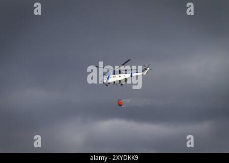 Die Brandbekämpfung Helikopter mit Bambi Korb mit Wasser auf dem Weg zu einem Brand geladen Stockfoto