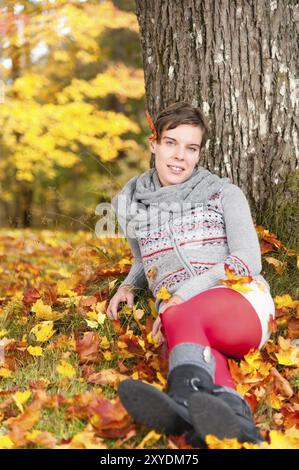 Eine attackierte junge Frau lehnt sich an einen Baum in lebhaftem gelbem und rotem Herbstlaub Stockfoto