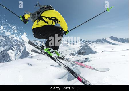 Ein Skifahrer in voller Sportausrüstung springt von der Spitze des Gletschers in den Abgrund vor dem Hintergrund des blauen Himmels und der kaukasischen Schneedecke Stockfoto