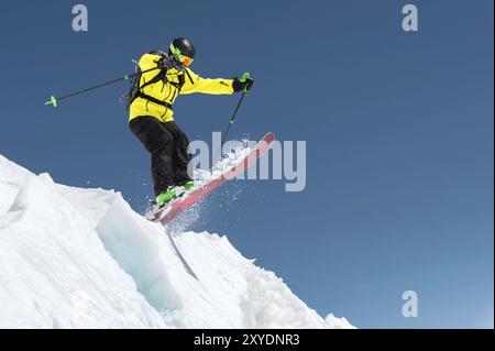 Ein Skifahrer in voller Sportausrüstung springt von der Spitze des Gletschers in den Abgrund vor dem Hintergrund des blauen Himmels und der kaukasischen Schnee-Ca Stockfoto