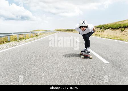 Der Typ mit Helm und Sonnenbrille fährt sehr schnell auf der Asphaltstraße in einem speziellen Sportständer sein Longboard Stockfoto