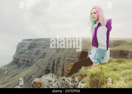 Ein Mädchen-Reisende mit bunten Haaren sitzt am Rande einer Klippe und blickt auf den Horizont auf einem Hintergrund eines felsigen Plateau Stockfoto