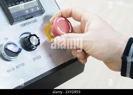 Nahaufnahme der Hand eines Mannes auf einer roten Taste auf dem Bedienfeld. Not-aus oder Start der Anlage und Produktion Stockfoto