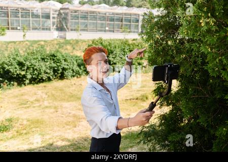 Frau mit orangefarbenen Haaren filmt sich am Telefon um Baum auf dem Campus Stockfoto