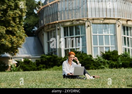 Ein Lehrer arbeitet an einem Laptop auf dem grünen Gras eines College-Campus. Stockfoto