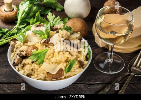 Risotto ai Funghi, Pilze Reis mit Zutaten und einem Glas Weißwein auf einem dunklen Holzmöbeln im Landhausstil Hintergrund Stockfoto