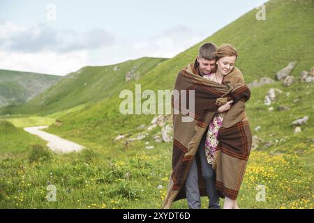 Porträt eines Mannes mit einem Mädchen, das mit einem Teppich bedeckt ist, umarmt eine Landstraße und lächelt vor Glück Stockfoto