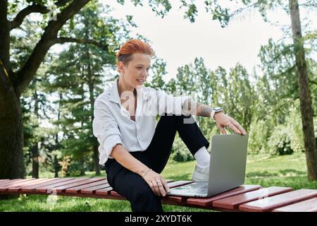 Ein Lehrer sitzt auf einer Bank und benutzt einen Laptop in einer friedlichen Parklandschaft. Stockfoto