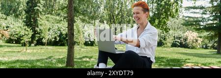 Ein Lehrer sitzt auf einer Bank und benutzt einen Laptop im Park. Stockfoto