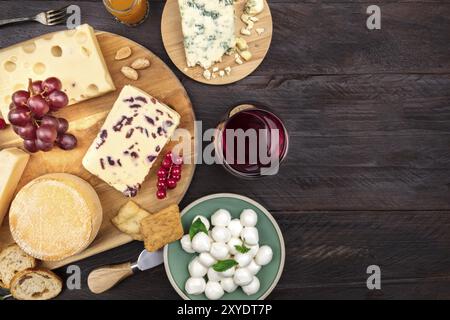 Ein Sortiment von verschiedenen Arten von Käse mit Wein und Trauben, geschossen von oben auf einem dunklen Hintergrund im Landhausstil mit einem Platz für Text Stockfoto