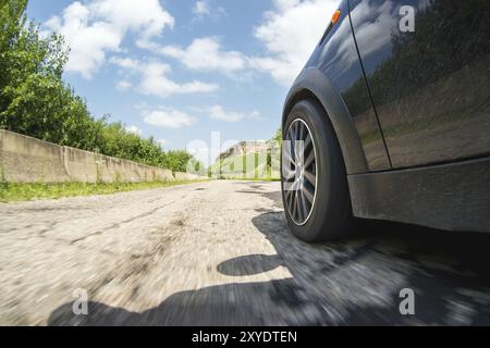 Eine Nahaufnahme der Seite des Autos und ein drehendes Rad, das mit hoher Geschwindigkeit auf dem Asphalt vor dem Hintergrund einer grauen Straßenlandschaft fährt Stockfoto