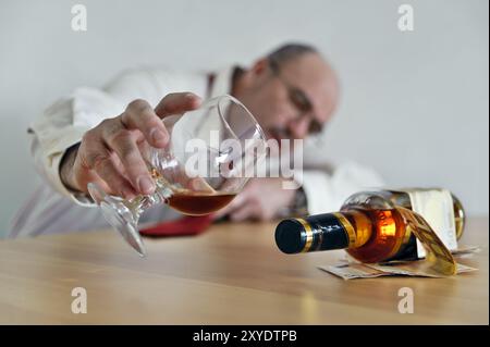 Mann mit Schussglas und Schnapsflasche, der an einem Tisch sitzt Stockfoto