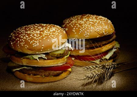 Zwei appetitliche Hamburger und Weizenohren zum Absacken. Landhausessen hell lackiertes Stillleben auf Schwarz Stockfoto