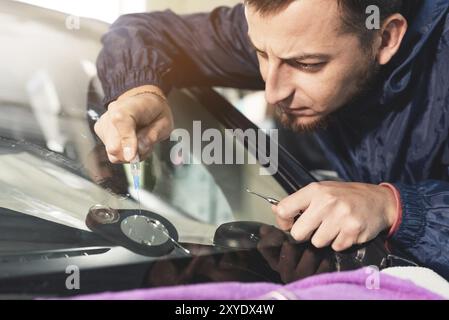 Nahaufnahme eines professionellen Windschutzscheibenreparateurs füllt einen Riss im Glas mit einem speziellen Polymer durch eine Spritze. Beseitigung von Rissen und Spänen o Stockfoto