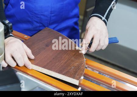 Ein professioneller Zimmermann verarbeitet die Kunststoffkanten der Arbeitsplatte mit einem Messerkantenschnitt. Das Konzept der Möbelproduktion Stockfoto