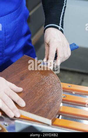 Ein professioneller Zimmermann verarbeitet die Kunststoffkanten der Arbeitsplatte mit einem Messerkantenschnitt. Das Konzept der Möbelproduktion Stockfoto