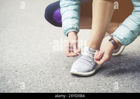 Läuferin, die Schnürsenkel bindet, um ihre Schuhe auf der Straße im Park zu joggen. Laufschuhe, Schnürsenkel. Übungskonzept. Sportlicher Lifestyle. Vintage-Style Stockfoto