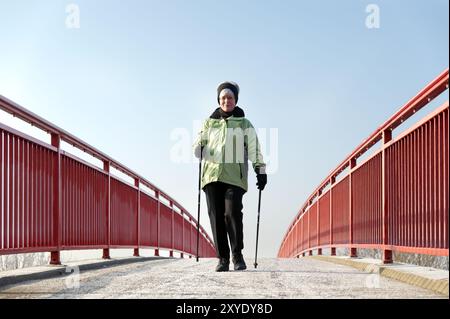 Frau Nordic, die über eine Brücke läuft, mit einem roten Geländer Stockfoto