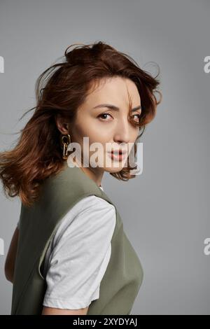 Eine schöne asiatische Frau mit langen braunen Haaren, die eine grüne Weste trägt, posiert vor grauem Hintergrund. Stockfoto