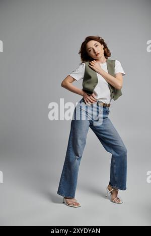 Eine stilvolle asiatische Frau posiert vor grauem Hintergrund. Sie trägt eine Weste und Jeans. Stockfoto