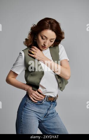 Eine stilvolle asiatische Frau posiert in einer grünen Weste, einem weißen T-Shirt und einer blauen Jeans vor grauem Hintergrund. Stockfoto