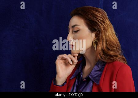 Eine Frau in rotem Anzug und Seidenhemd posiert vor dunklem Hintergrund. Stockfoto