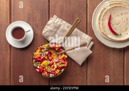 Huevos Rancheros, mexikanische gebackene Eier, von oben mit Pico de gallo Salat, heißer Schokolade und Tortillas auf einem dunklen rustikalen hölzernen Hintergrund mit geschossen Stockfoto