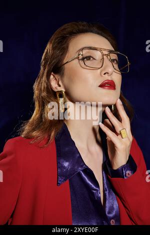 Eine asiatische Frau in rotem Anzug und Seidenhemd blickt selbstbewusst nach oben, ihr Goldschmuck fällt ins Licht. Stockfoto