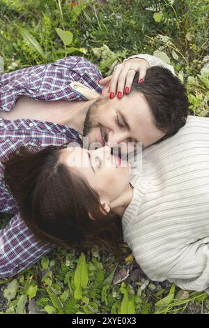 Ein liebevolles Paar Hipster liegt in einer Umarmung auf dem Gras und streichelt sich gegenseitig Stockfoto