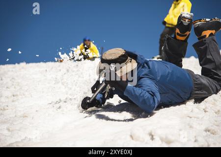 Training zum Korrigieren des Rutschens an Hanglagen oder Gletschern mit Hilfe einer Eispistole. Ein voll ausgestatteter Backpacker rutscht auf dem Bauch entlang einer verschneiten Piste in Th Stockfoto